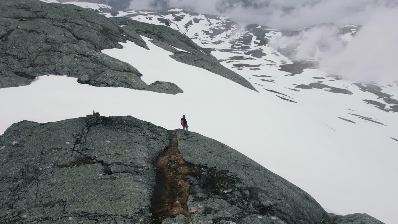 vista aérea de un excursionista caminando por el borde de la repisa de la montaña ishaug de la tienda con vistas al paisaje cubierto de nieve en el parque nacional hardangervidda, eidfjord, noruega