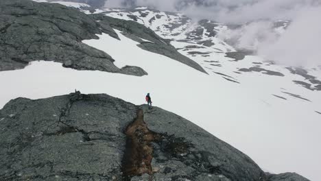 aerial view of hiker walking along edge of store ishaug mountain ledge looking over snow covered landscape at hardangervidda national park, eidfjord, norway