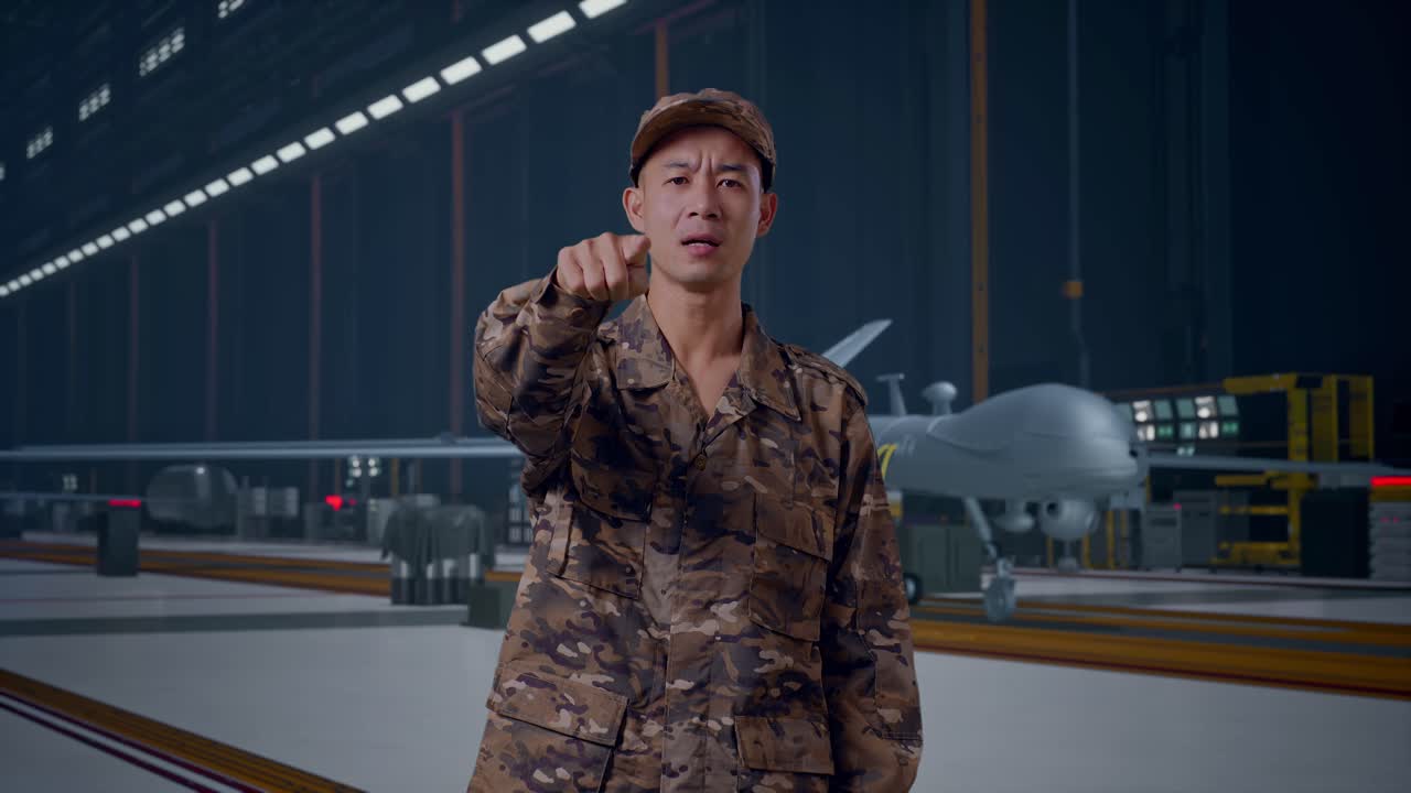 Uomo soldato asiatico che grida alla telecamera mentre è in piedi con un moderno drone militare in un hangar di manutenzione