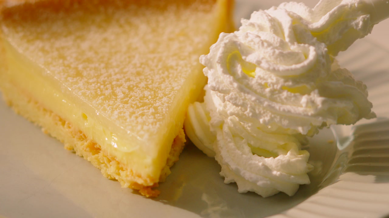 Crème fouettée placée sur une assiette avec une tarte au citron française classique, sous lumière naturelle. Idéal pour les applications culinaires, les montages pour les réseaux sociaux et les promotions de restaurants haut de gamme. 4K.