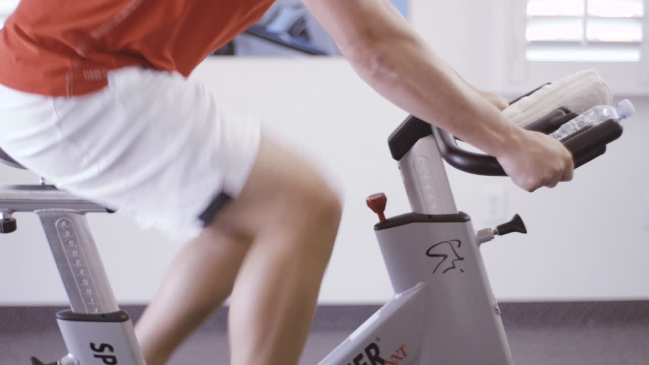 Man is engaged in a bicycle simulator in the gym. The guy is exercising on a stationary bike.