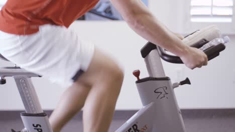 man is engaged in a bicycle simulator in the gym. the guy is exercising on a stationary bike.