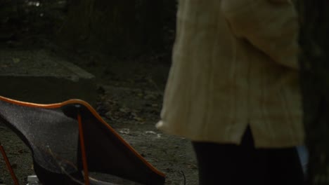 female walks past camping chairs and camp fire burning outside