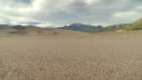 cinematic push in close up of sandy desert with pull focus revealing the background mountain range