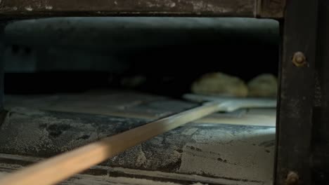 shot of inside oven, baker’s peel going out with some crusty and goldy loaf bread