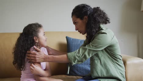 madre de raza mixta aconsejando a su hija en el sofá de la sala de estar