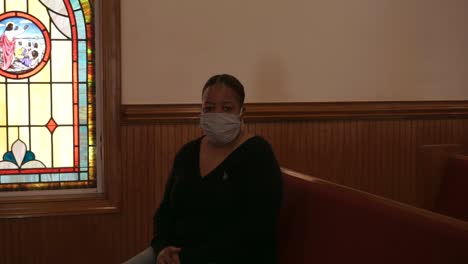 black african american woman sitting in empty church during pandemic wearing mask looking directly at camera