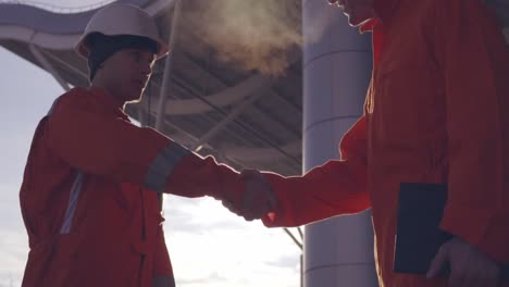 close up view of two construction workers in orange uniform and hardhats shaking hands at the building object