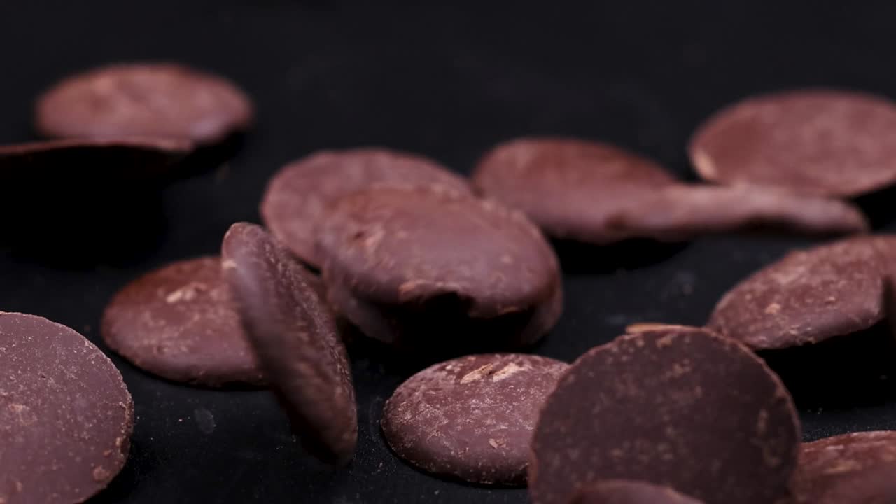 Chocolate discs landing and scattering on a dark surface, showcasing texture and movement in close-up detail.