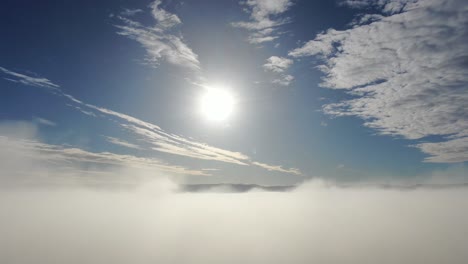 Aerial-flight-by-drone-over-an-unbroken-fog-layer-on-a-beautiful-blue-sky-day-with-mottled-clouds