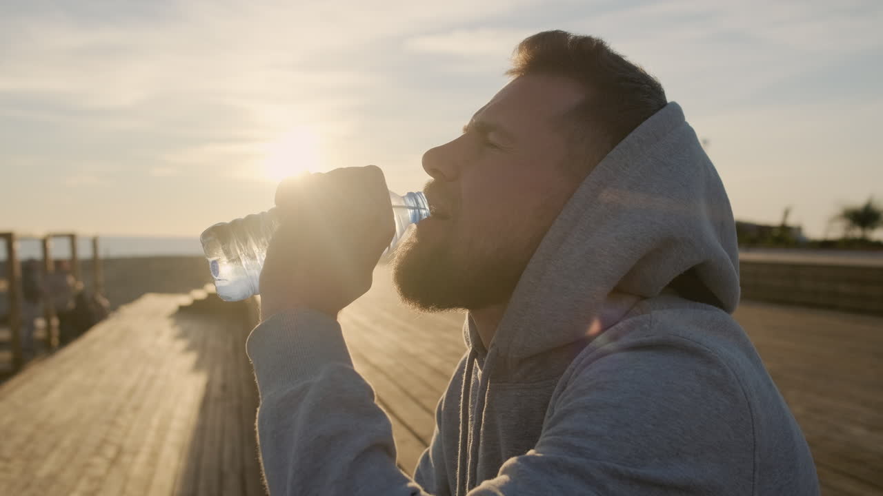해가 지면 해변에서 물을 마시는 남자