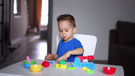 adorable caucasian baby boy sits at desk in his room. little toddler kid plays with plasticine.