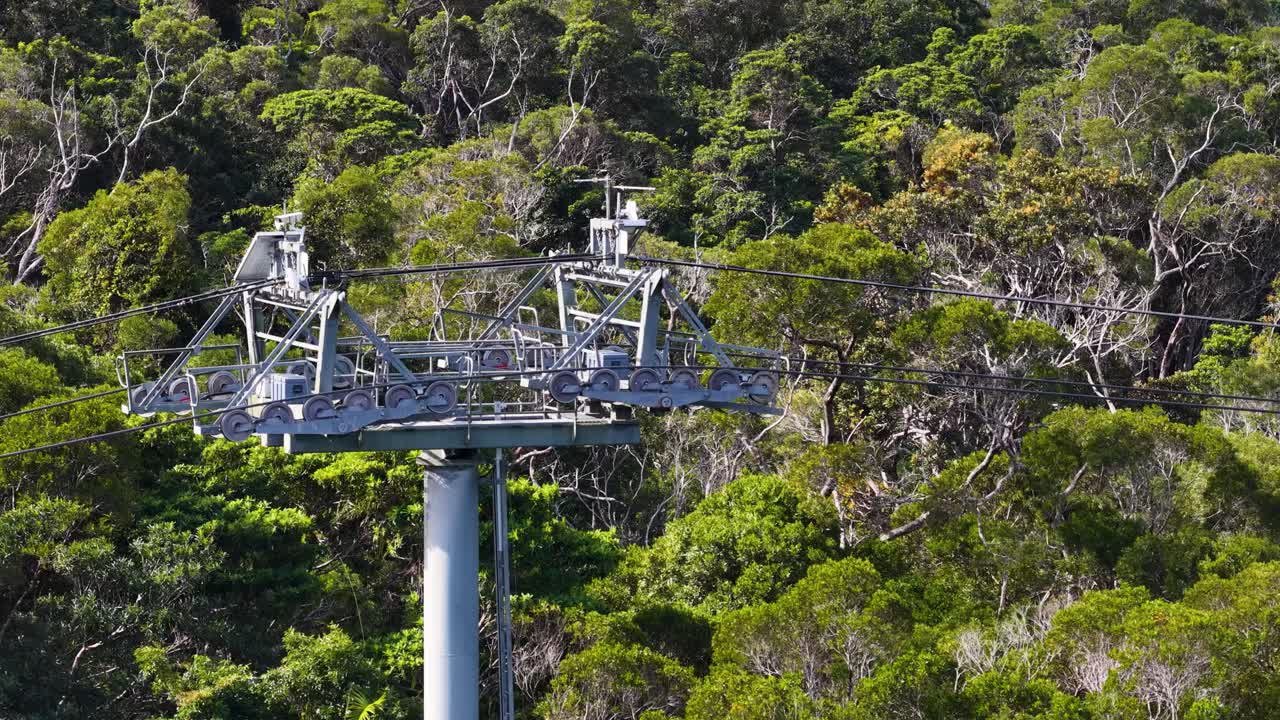 Drone captures cable car structure above dense rainforest, showcasing metal framework and vibrant greenery in natural light