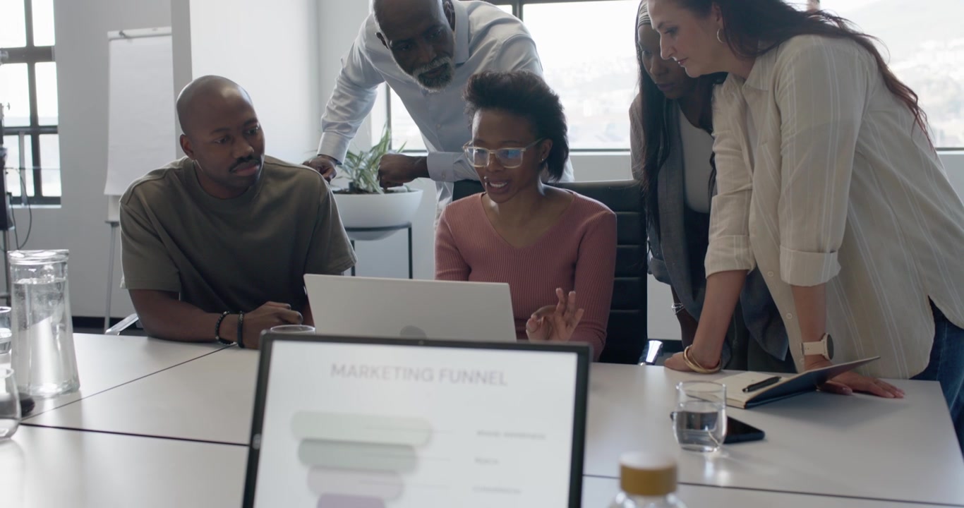 Diverse team gathering as presenter clicking laptop, reviewing marketing funnel in office