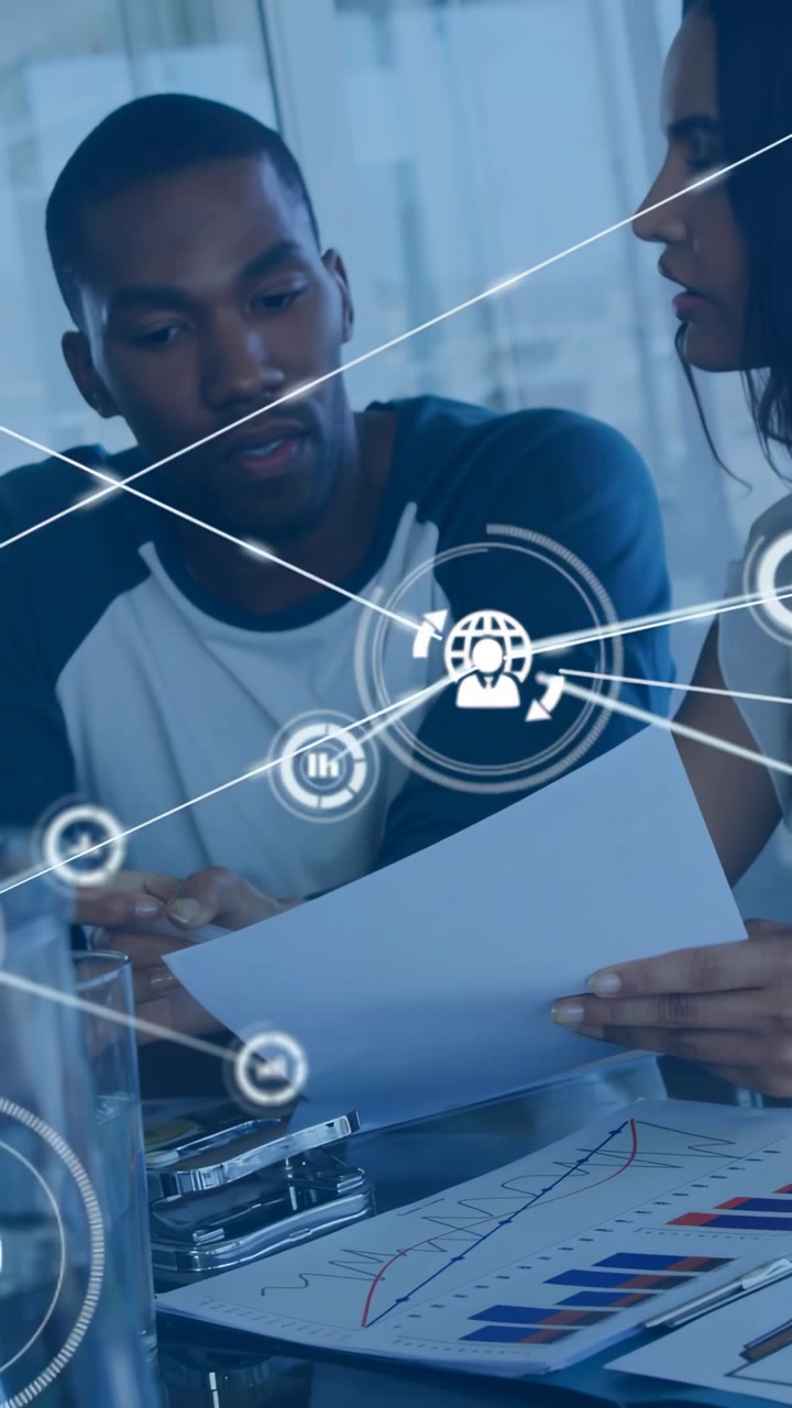 Vertical video: Two peers reviewing charts in business, starting AR icons multiplying over paper
