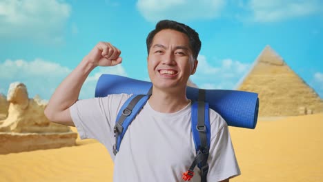 close up of asian male hiker with mountaineering backpack smiling and flexing his bicep while traveling in pyramid of giza