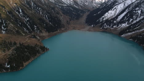 aerial shot tilting over the big almaty lake, revealing snowy mountains of kazakhstan