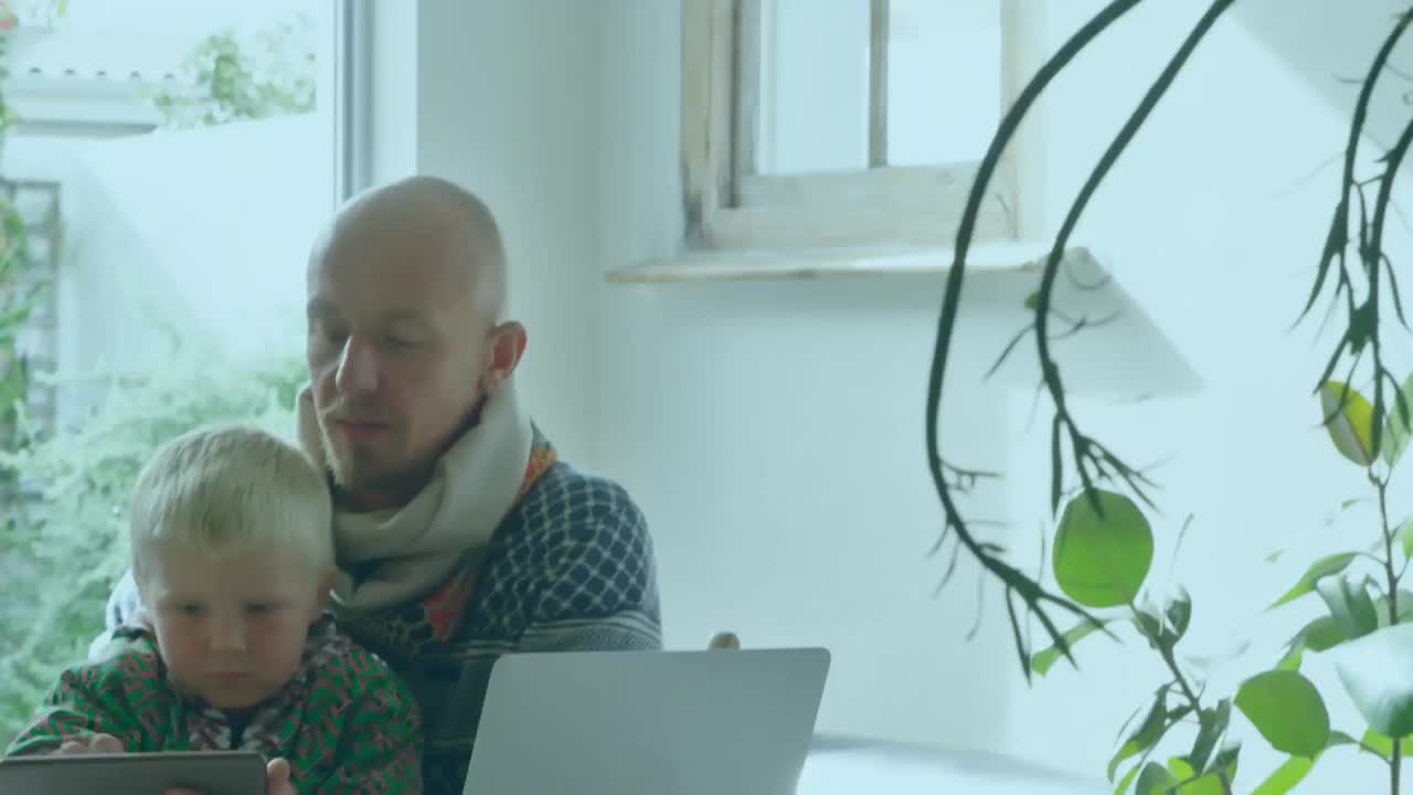 Animation of words Stay At Home over Caucasian man with kid Using his lapto