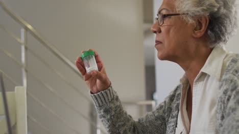 African-american-senior-woman-holding-medication-container-having-a-video-call-on-laptop-at-home