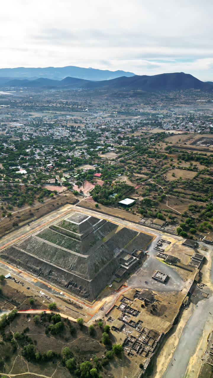 Aerial drone view of the ancient Teotihuacan pyramids with the surrounding Mexican town and mountain landscape. Vertical