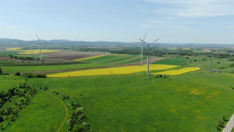 Wind-turbines-producing-renewable-energy-on-green-and-golden-fields-of-European-countryside,-aerial