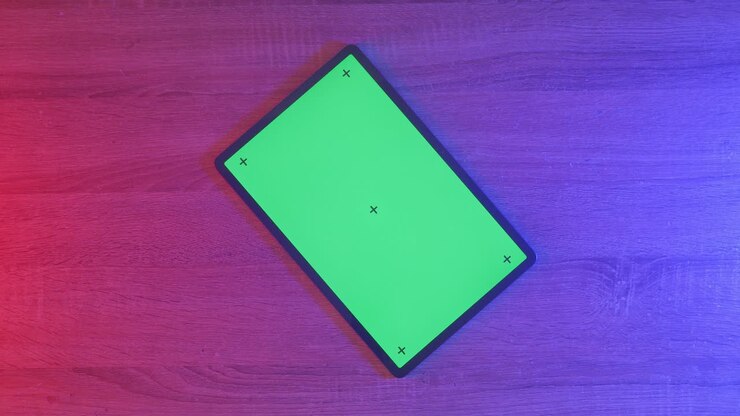 Tablet con schermo verde su tavolo di legno sotto luce rosa e blu