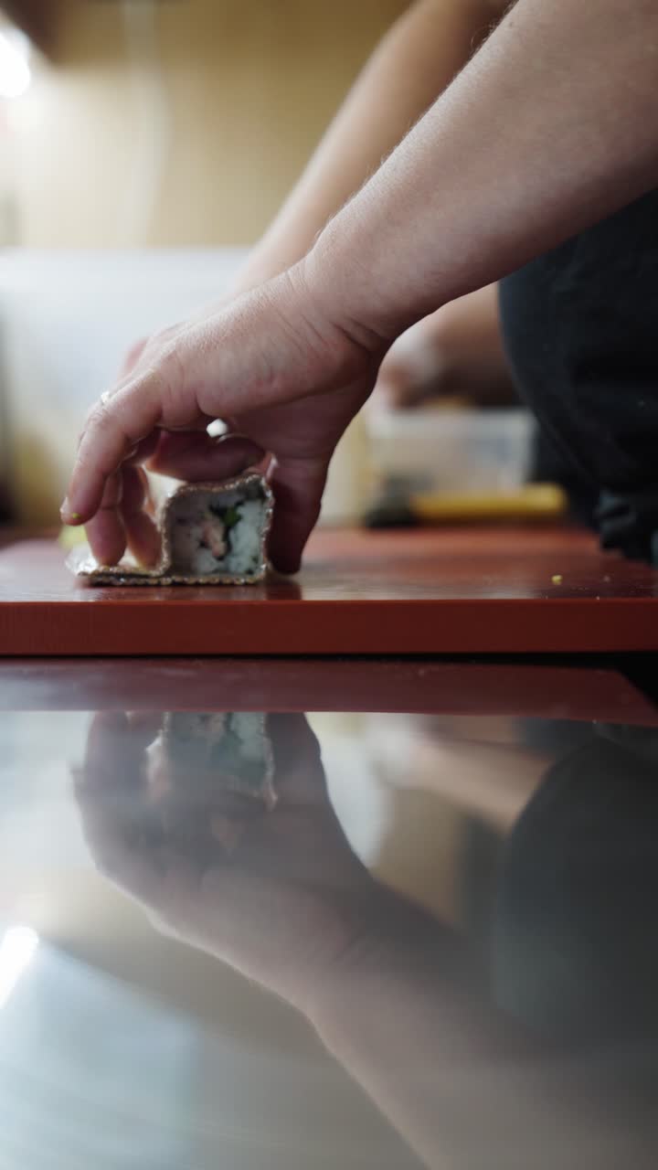Vertical close up of chef hands shape urumaki sushi roll with bamboo wrapper