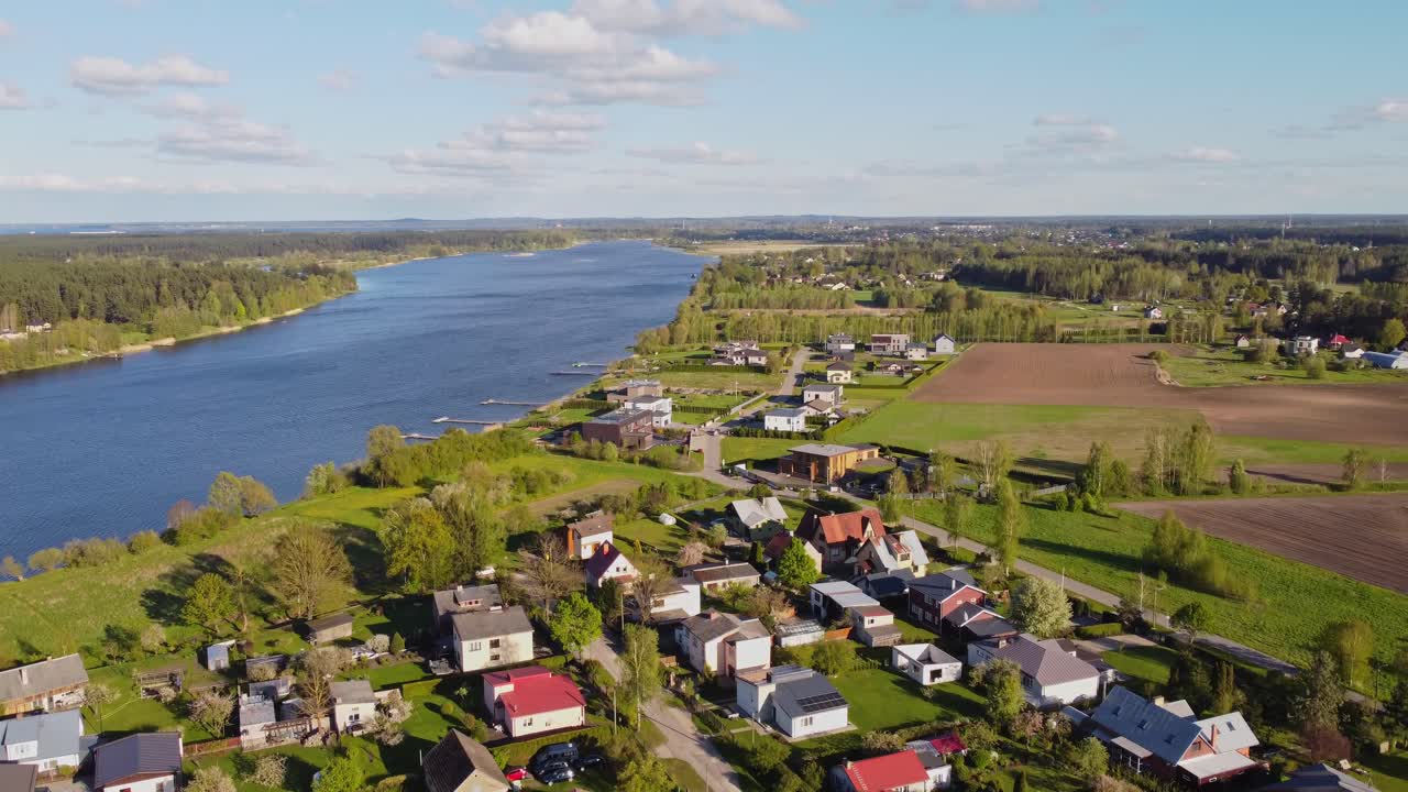 Vertical camera movement reveals the sunny Katlakalns Spring area beside a wide river in Latvia.