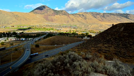 hiperlapso de tiro panorámico a la derecha de los puentes en la autopista 1 y la autopista 5 de cabeza amarilla en kamloops bc canadá, con automóviles y semirremolques conduciendo, el monte paul en el fondo y la vegetación del desierto al frente