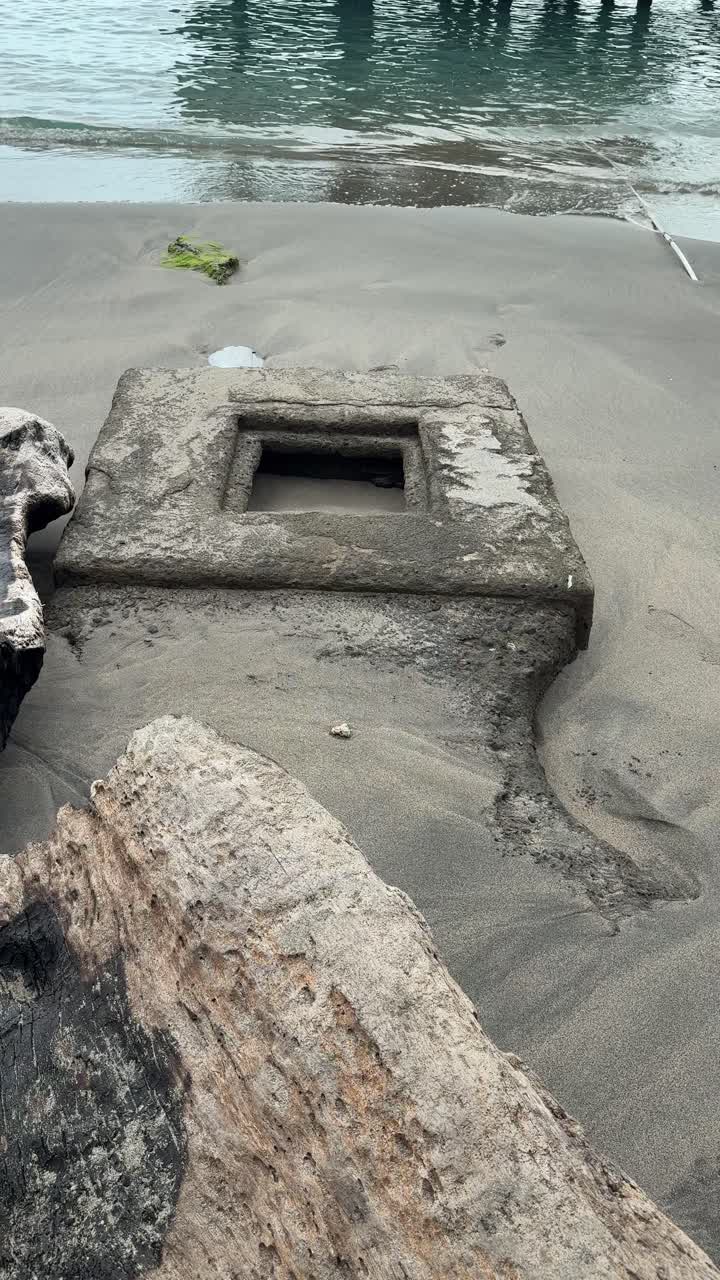 Værbitt drivved og betongkonstruksjon på en rolig sandstrand