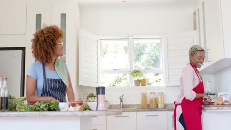 happy diverse female lesbian couple wearing aprons and cooking in kitchen in slow motion