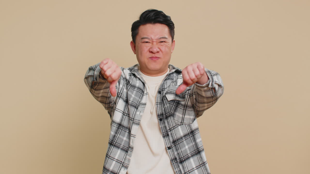 Upset asian man guy showing thumbs down gesture disapproval dissatisfied dislike negative feedback