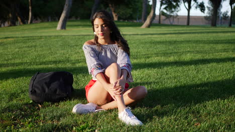 beautiful young hispanic college student resting on a grassy park field between classes on campus