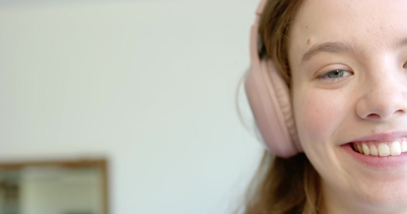 Donna che indossa cuffie over-ear rosa apre gli occhi e sorride a casa, con un quadro incorniciato.