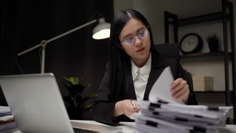 young asian business woman working at late night. she was very busy checking paperwork and had to send the work before the deadline, feeling stressed. sitting in the dark office at night.