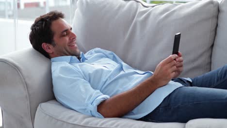 casual man lying on the sofa sending a text message