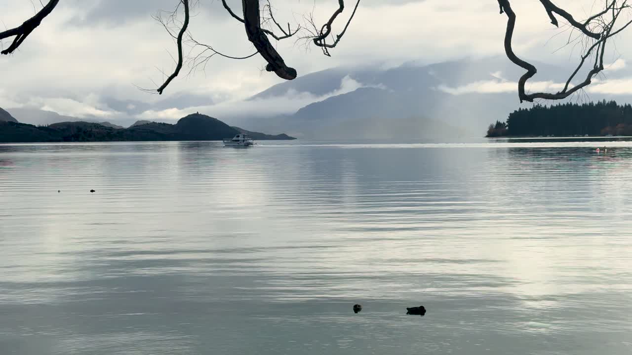Calm waters and distant mountains under cloudy skies at Lake Wanaka, New Zealand. Tranquil and reflective atmosphere