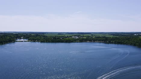 an establishing shot of a drone flying over a speed boat boating across killarney turtle mountain lake during the summer in south west manitoba canada