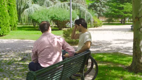 disabled young man sits in his wheelchair and talks to his friend outdoors in slow motion.