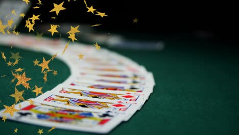Composite-video-of-multiple-golden-star-icons-falling-against-playing-cards-on-green-surface