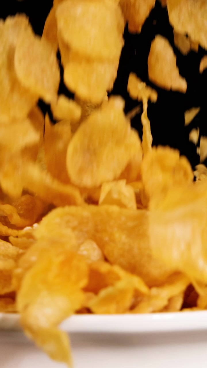 Fiocchi di mais cadono a cascata in una ciotola bianca su uno sfondo nero, creando una scena dinamica e visivamente suggestiva.