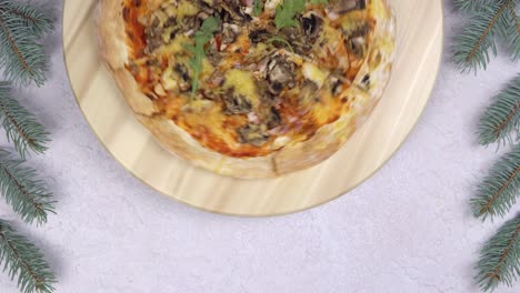 una capa plana de pizza girando una rotación de 360 grados en un salvador de madera, con decoraciones navideñas a su alrededor.