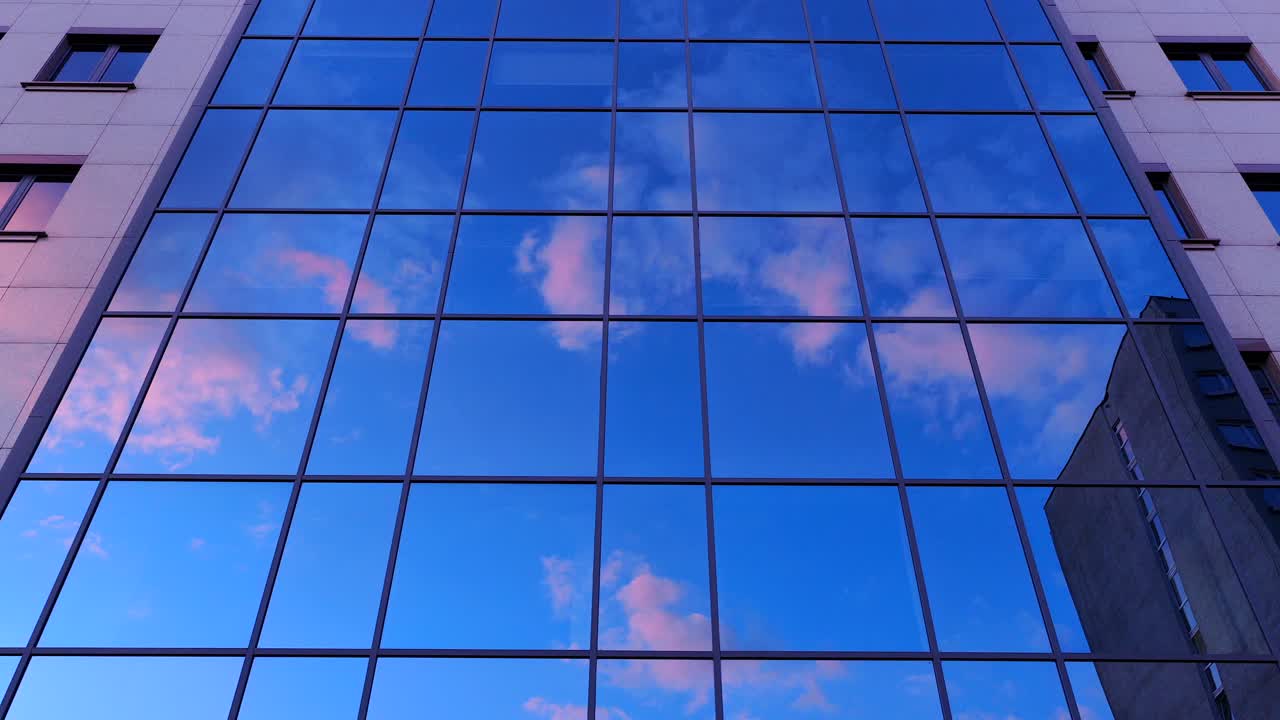 Drone footage glides past a modern glass building in Warsaw, Poland, reflecting vibrant blue skies and soft clouds—ideal for themes of architecture, innovation, or urban lifestyle