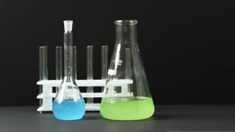 Coloured-liquids-in-flasks-with-test-tubes-in-stand-on-black-background-with-copy-space,-slow-motion