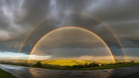 a stunning double rainbow arches over lush green hills beneath dramatic skies, creating a magical landscape that captivates the viewer with its beauty and wonder