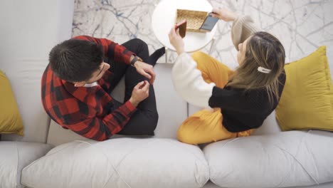 una joven pareja se sienta incrustada en los teléfonos inteligentes e ignora el uno al otro.