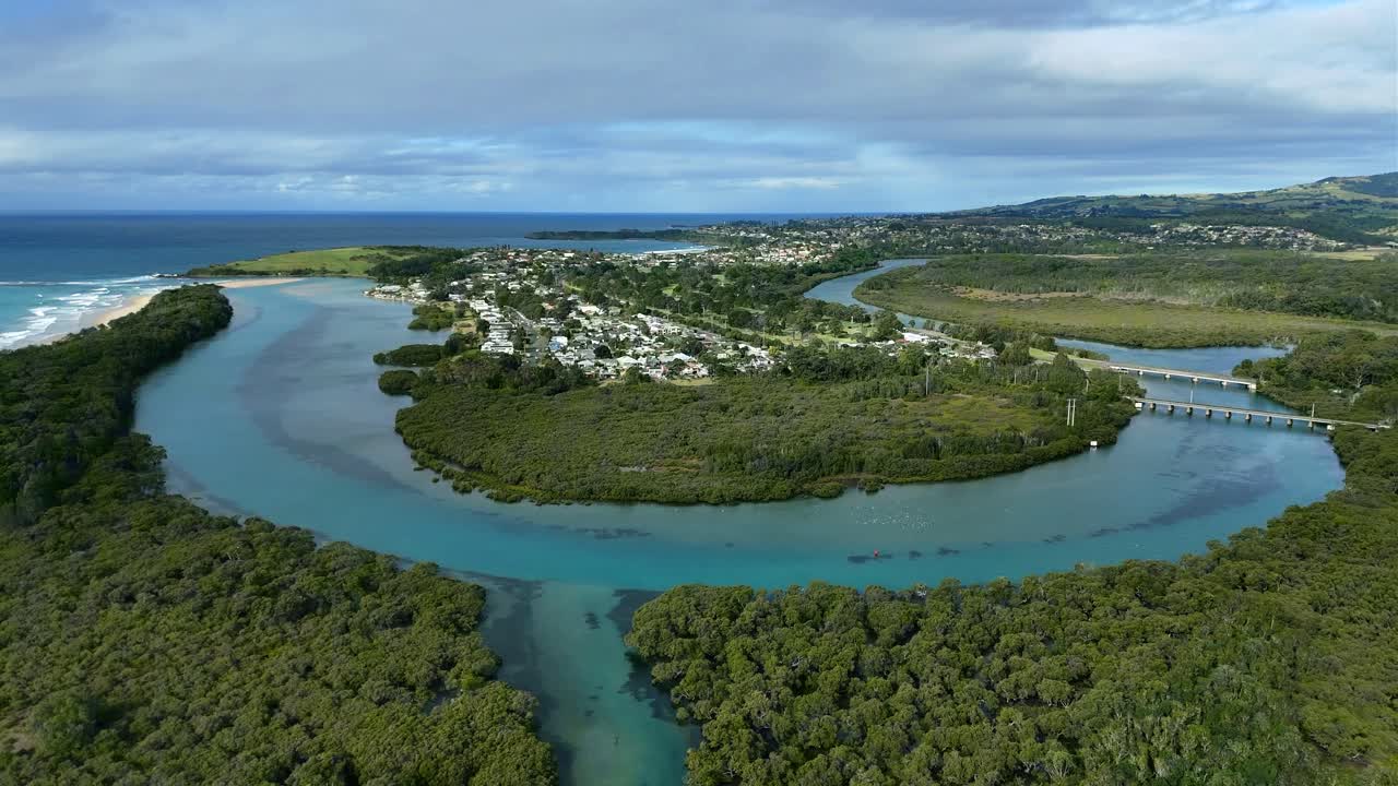 Aerial panoramic pullback showing looping bends of Minnamurra River cutting through vibrant estuarine landscape near homes