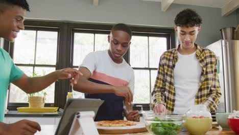 Happy diverse male teenage friends preparing pizza in kitchen, slow motion