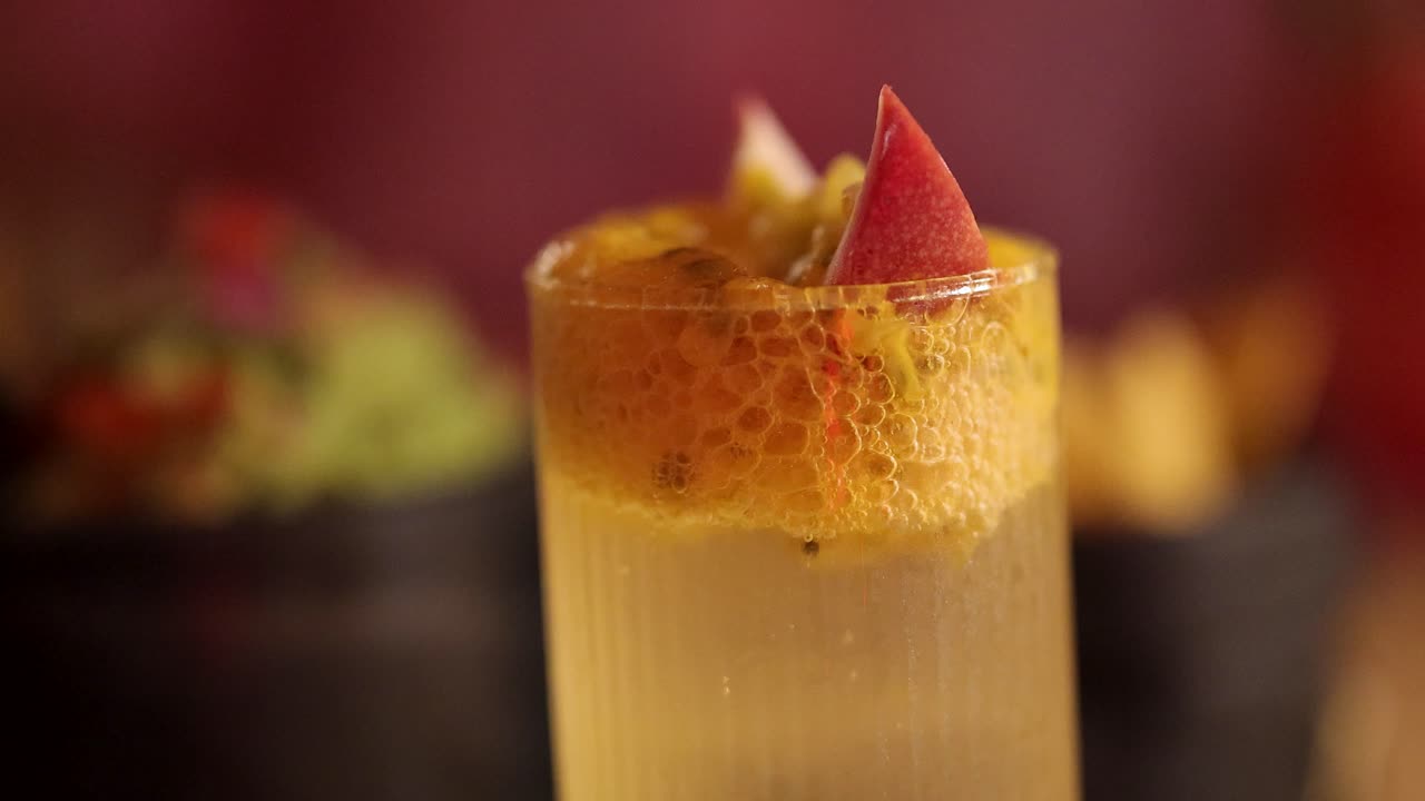 A vibrant passion fruit cocktail garnished with fruit slices, set in a lively Bangkok restaurant with warm lighting