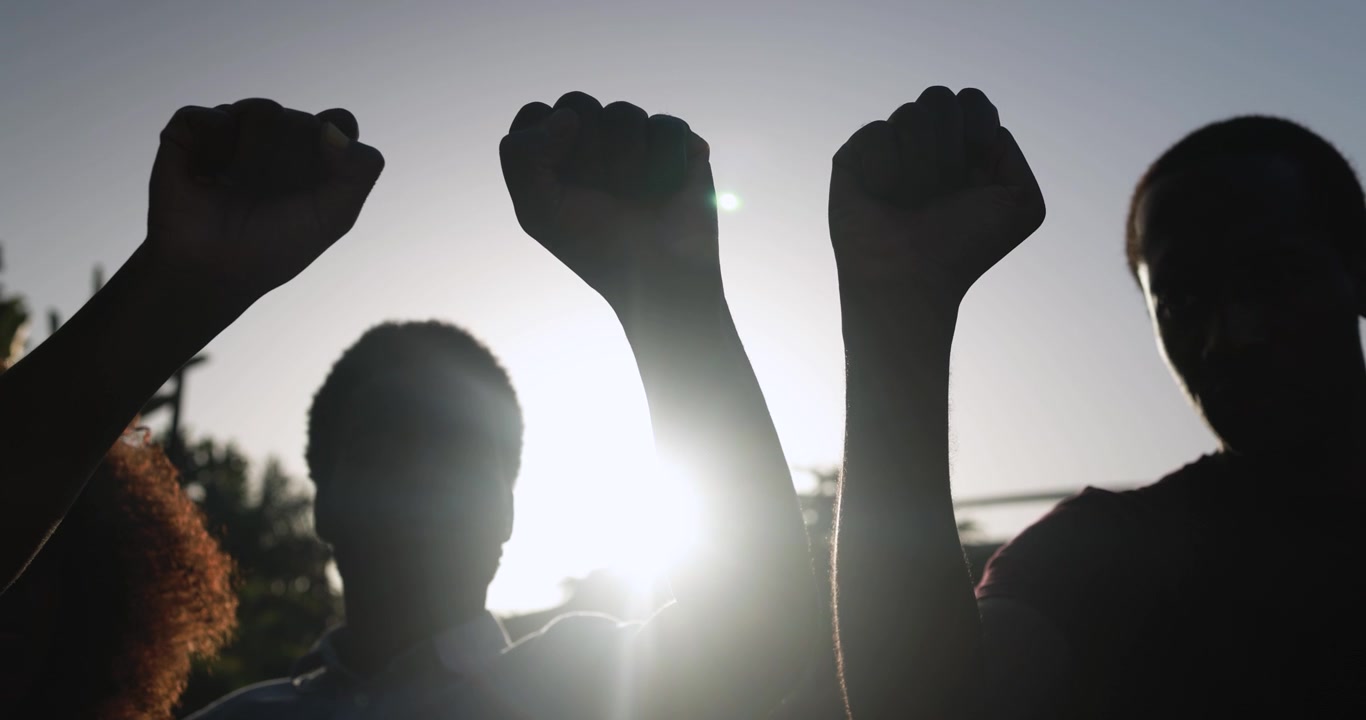 Sagome di persone che alzano i pugni in protesta contro un cielo luminoso